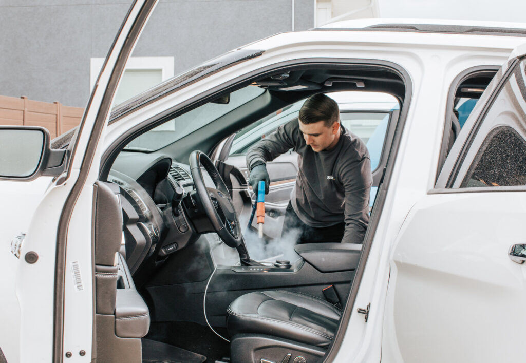 Employee steam-cleaning car interior